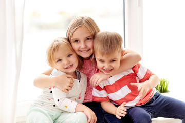 childhood, leisure and family concept - happy little kids hugging at window