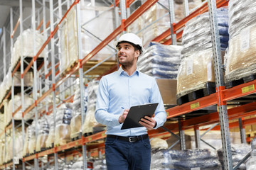 Wall Mural - logistic business, shipment and people concept - businessman in helmet with clipboard checking goods at warehouse