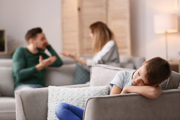 Wall Mural - Little unhappy boy sitting in armchair while parents arguing at home