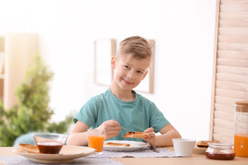 Wall Mural - Cute little boy spreading jam onto tasty toasted bread at table