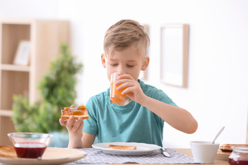 Wall Mural - Cute little boy eating tasty toasted bread with jam at table