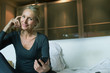 © PhotoAlto - Mature sitting on bed with smartphone in hand, smiling, portrait
