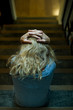 © PhotoAlto - Woman sitting on stairs with hands clasped on head, rear view