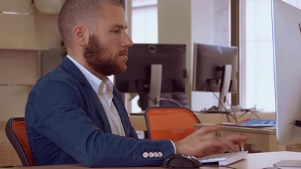 Poster - handsome caucasian man with beard sitting at the workspace typing on keyboard looking on screen computer. employee focused at work