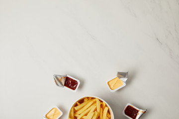 Wall Mural - top view of french fries in bowl surrounded with containers of sauces on white