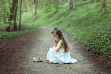 Little girl with small rabbit in the forest.