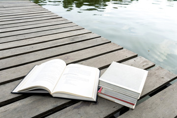 Books on the wood floor the bridge of waterside area adjoining lake or river in nature forest background with copy space for text. Concept for education.