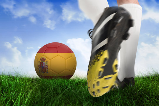 Composite image of football boot kicking spain ball against field of grass under blue sky