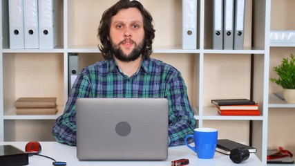 Poster - handsome it man sitting at the workspace looking at the camera with friendly smile talking with view
