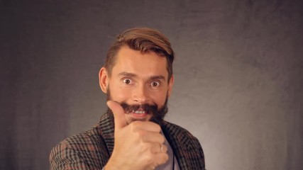 Leinwandbilder - portrait young man with beard posing on background in studio. handsome caucasian guy wearing casual shirt and trendy jacket. happy millennial looking at the camera showing hand gesture like approval