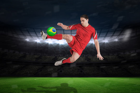 Fit football player jumping and kicking against large football stadium with fans in yellow