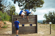 © WavebreakmediaMicro - Female trainer assisting fit man to climb over wooden wall during obstacle course