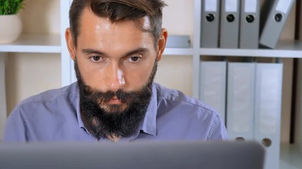 Poster - close up portrait bearded man working with computer in office. handsome man focused at screen laptop than looking at the camera