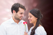 Handsome man offering his girlfriend a rose against valentines heart design
