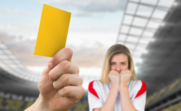 Hand holding up yellow card against football stadium with fan