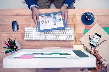 Fototapete - Business graphs against businessman holding digital tablet while sitting at computer desk 