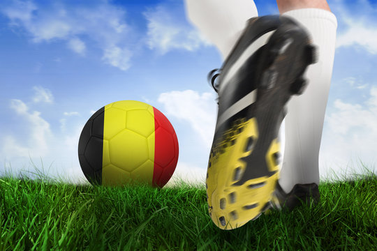 Composite image of football boot kicking belgium ball against field of grass under blue sky