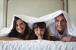 © WavebreakmediaMicro - Happy family lying under blanket on bed at home
