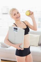 Poster - Fit woman in sportswear holding scale and apple in fitness studio