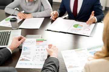 Close-up of financiers and investors discussing company development while viewing results of survey and business analysis at meeting