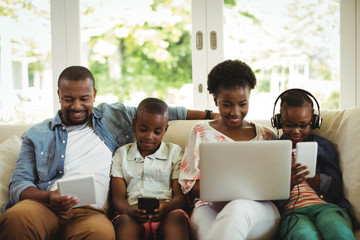 Wall Mural - Parents and kids using laptop, smartphone and digital tablet on sofa