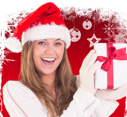 Festive blonde holding a gift against fir trees with snow flakes