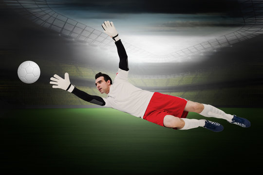 Goalkeeper in white making a save in a large football stadium with lights