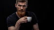 Closeup shot of bearded man drinking coffee and looking at camera Sitting handsome perfect hairstyle man drinking espresso holding cup of coffee in hand Studio shot on black background.