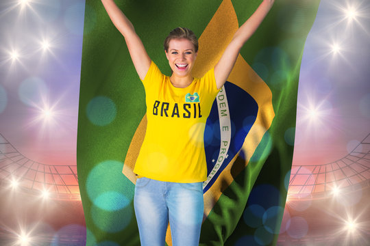 Excited football fan in brasil tshirt holding brasil flag against large football stadium under purple sky