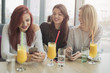 © Mateja88 - Portrait of three young beautiful women using mobile phone at coffee shop.