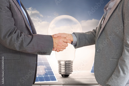 Poster Close up on two businesspeople shaking hands against light bulb and solar panels