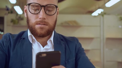 Poster - portrait adult businessman using smart phone messaging indoors. handsome man with red beard wearing casual jacket texting message at work or cafe chatting or sharing something or checking email or buy
