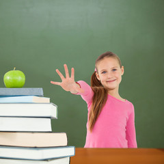 Cute girl with hand out against green apple on pile of books in classroom