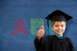 Cute pupil in graduation robe against blue chalkboard with abc