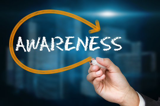 Businessman writing the word awareness against shiny cityscape on black background