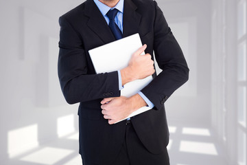 Canvas Print - Smiling businessman holding his laptop looking at camera against white room with squares at wall