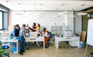 open plan room with mixed race energetic students giving high five to each other. copy-space