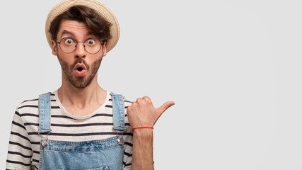 Wall Mural - Portrait of handsome bearded male farmer being shocked as has much work about house in ranch, points with surprising expression at blank copy space for your advertisement. People and agriculture