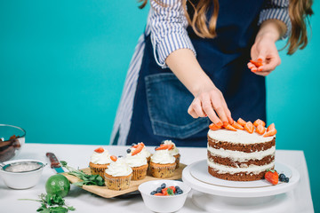 Cropped view of womans hands putting strawberries on cake