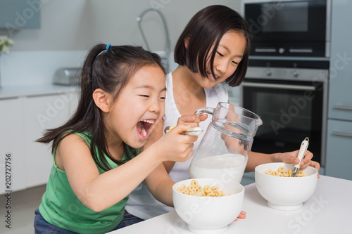 Fotografia, Obraz Two happy young girls eating cereals in kitchen