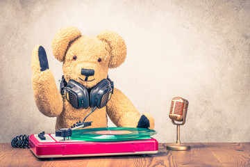 Wall Mural - Teddy Bear toy with old headphones at the retro DJ turntable mixer and microphone  on wooden table. Vintage style filtered photo