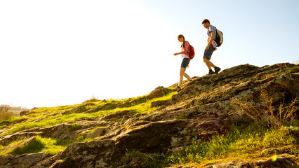 Wall Mural - young happy couple hiking with backpacks on the beautiful rocky trail at sunny evening. family trave
