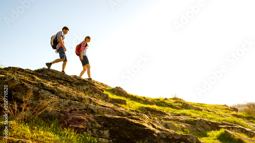 Fotografía Young Happy Couple Hiking with Backpacks on the Beautiful Rocky Trail at Sunny Evening