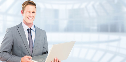 Poster - Happy businessman with laptop against modern room overlooking city