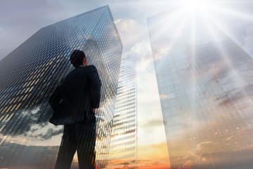 Canvas Print - Businessman standing with hands on hips against low angle view of skyscrapers at sunset