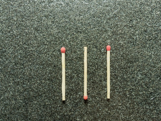 Three wooden match sticks with red head put in Y shape over black or dark granite texture with concepts of energy, old fashion, vintage, and retro