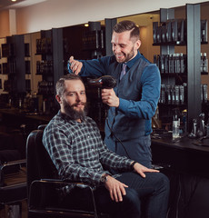 Professional barber working with a client in a hairdressing salon, uses a hair dryer.