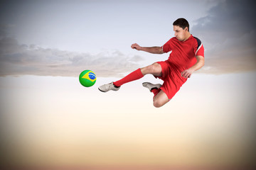 Fit football player jumping and kicking against beautiful orange and blue sky