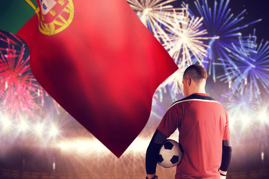 Goalkeeper in red holding the ball against fireworks exploding over football stadium