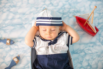 Wall Mural - Cute toddler baby boy sleeping in wooden boat with fishes, starfish and binoculars, dressed as sailman